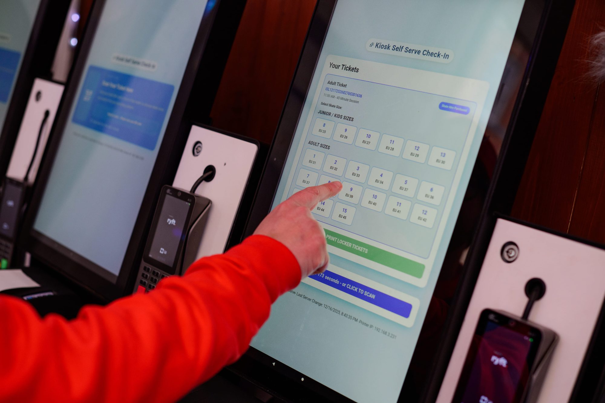 A finger selects a skate size on a kiosk check-in screen, with a card terminal mounted beside the screen.